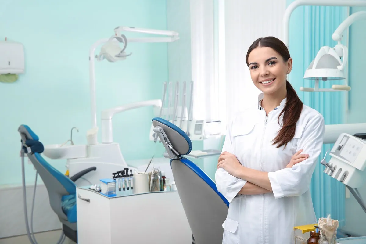 Young female dentist in white coat at workplace. Space for text