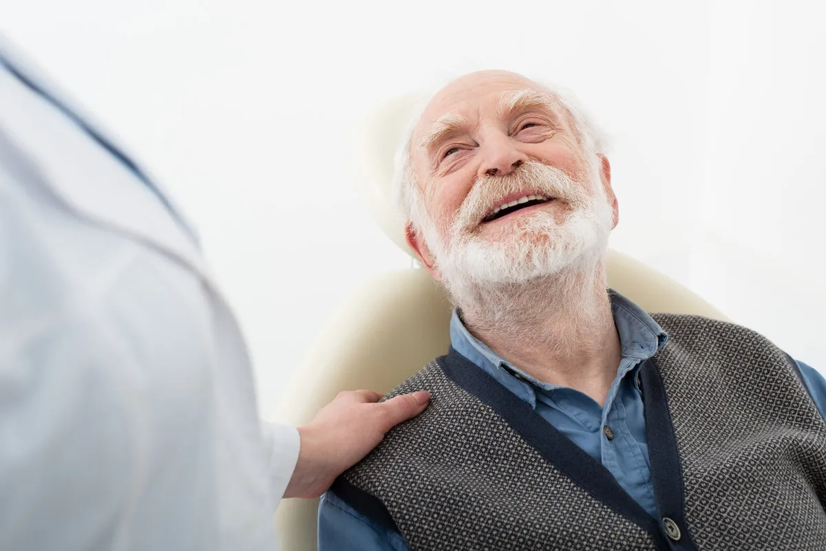 smiling senior patient sitting in dental chair with dentist hand on shoulder,stock image