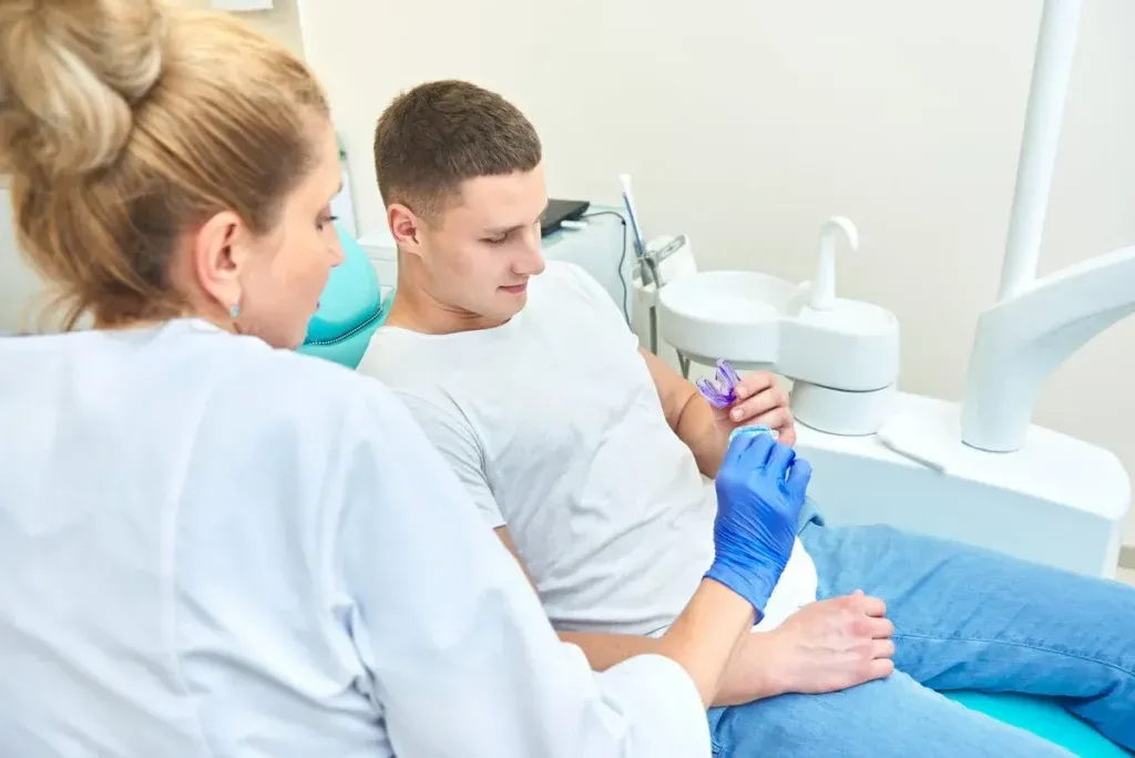 woman doctor dentist shows a mouth guard to a man. the patient sits in the dental chair in the office