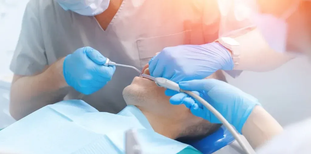 Dentist with assistant using equipment for examination of teeth of man patient. Dentistry clinic banner, young men getting dental checkup